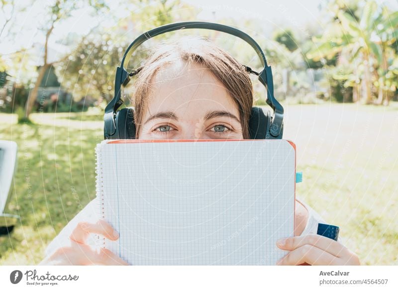 Young woman sitting on the garden smiling and studying for the university enjoys outdoor recreation hearing music and using a laptop. Copy space, People lifestyle concept. Typing on the computer