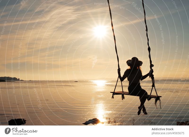 Unrecognizable woman sitting on swing over sea at sunset silhouette sundown spain cambados evening sky dusk nature enjoy relax rest twilight harmony summer