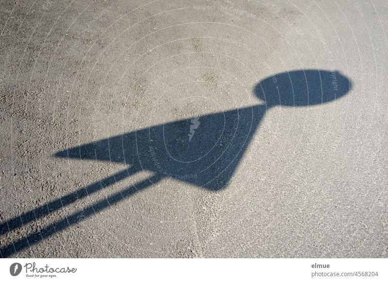 Shadow of a round and a triangular traffic sign on an asphalt road in the form of a toy man / optical illusion Road sign two little man shadow cast Asphalt