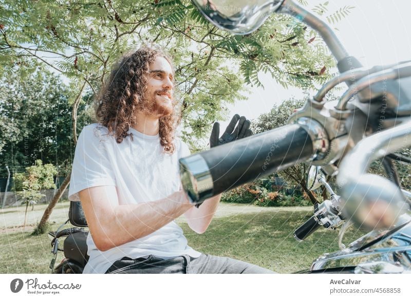 Portrait of a young long hair man in a motorbike using gloves doing a road trip. Travel concept. Gloves and rude hands holding a map over a old school motorbike.