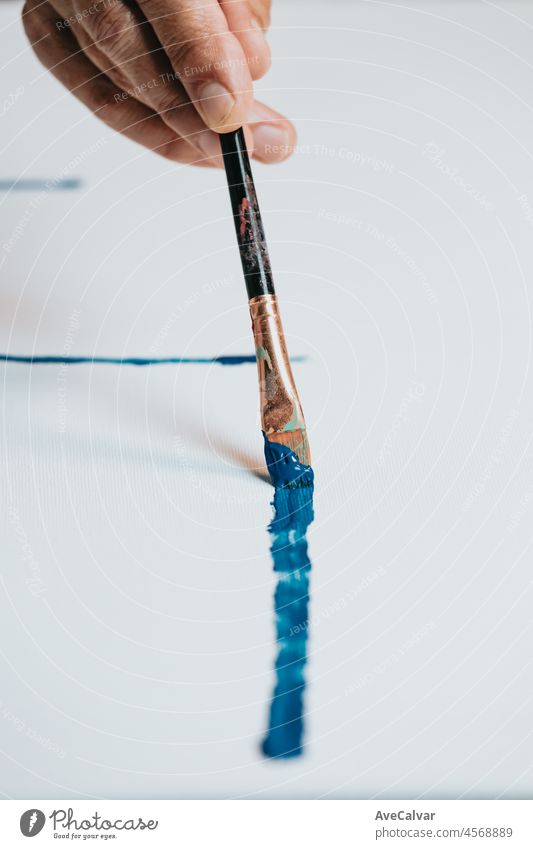 Close-up of Female senior old Artist Hand, Holding Paint Brush and Drawing Painting with blue Paint. Colorful, Emotional Oil Painting. Contemporary Painter Creating Modern Abstract Piece of Fine Art