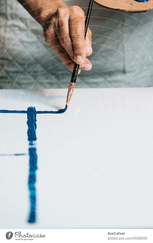 Close-up of Female senior old Artist Hand, Holding Paint Brush and Drawing Painting with blue Paint. Colorful, Emotional Oil Painting. Contemporary Painter Creating Modern Abstract Piece of Fine Art