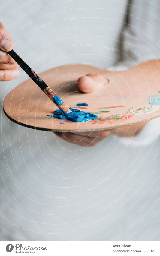 Close-up of Female senior old Artist Hand, Holding Paint Brush and Drawing Painting with blue Paint. Colorful, Emotional Oil Painting. Contemporary Painter Creating Modern Abstract Piece of Fine Art