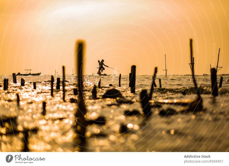 Unrecognizable fishermen on poles in sea fishing water work coastal evening collect rod rural environment wave people natural male job ocean equipment