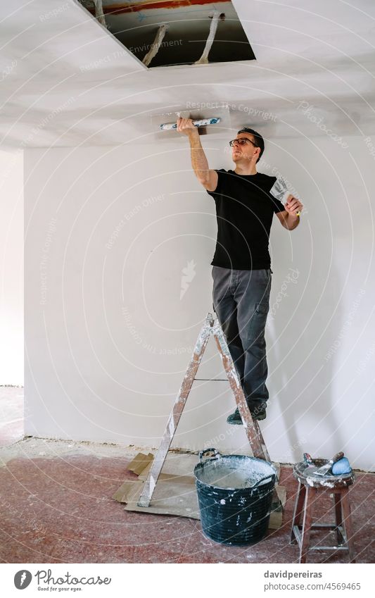 Plasterer smoothing plaster ceiling with the trowel mason builder professional plasterer climbed on ladder gypsum plaster gypsum board spatula working