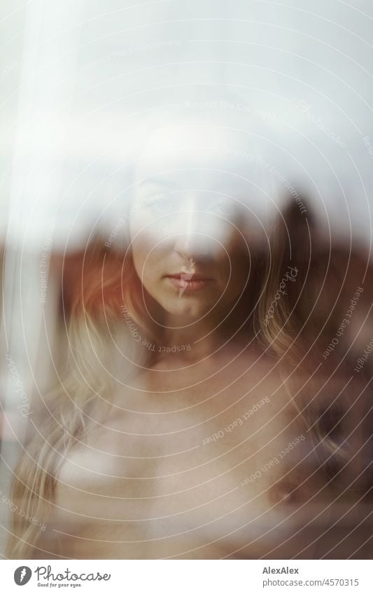 Nude portrait of a young, blond, long-haired woman looking naked into the camera behind the window pane Youthfulness salubriously Facial expression Warmth