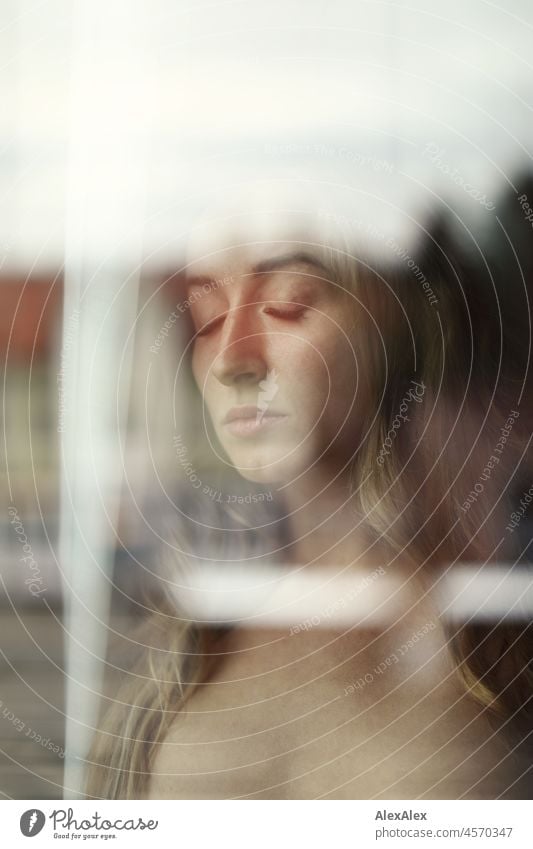 Nude portrait of a young, blond, long-haired woman standing naked and with closed eyes behind the window pane Youthfulness salubriously Facial expression Warmth