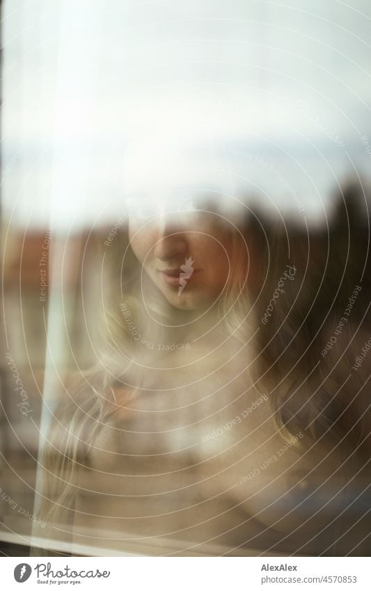 Nude portrait of a young, blond, long-haired woman looking naked into the camera behind the window pane Youthfulness salubriously Facial expression Warmth