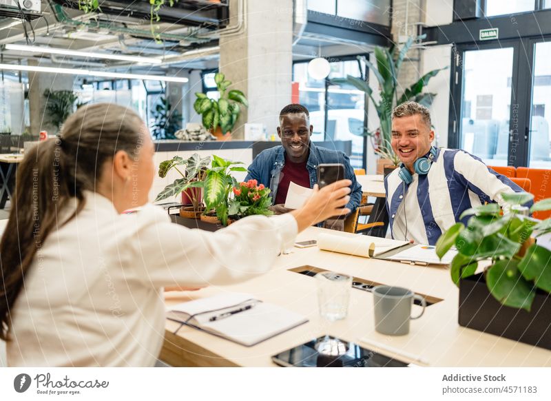 Woman showing information on smartphone to positive diverse colleagues businesspeople browsing amusement work online coworker office company workplace