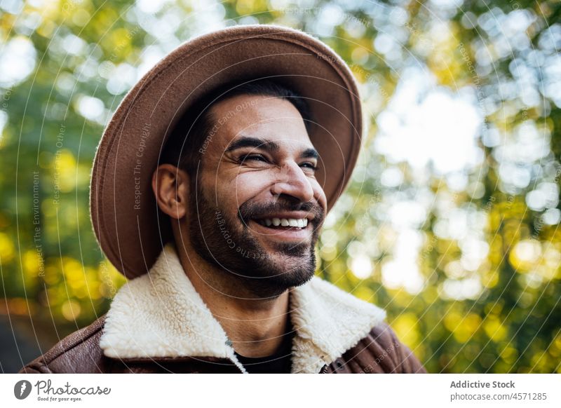 Happy hipster guy standing in woods with green trees man nature style grove adventure trip recreation leisure outfit trendy hat summer wear male apparel