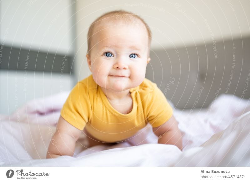 Caucasian blonde baby seven months old lying on bed at home. Kid wearing cute clothing yellow color newborn infant Illuminating child ultimate gray kid