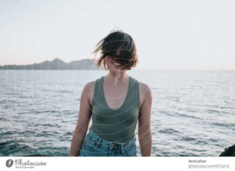 A young woman walks on the path of rocks on the shore and looks at the evening sea.Young hipster girl doing some hiking on the shore, traveling and low budget travel concepts, copy space