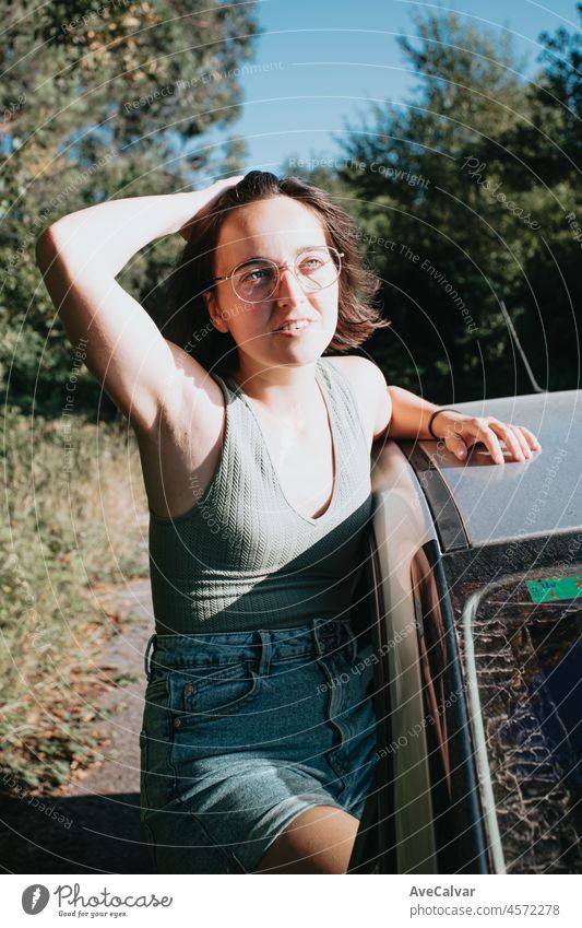 Beautiful Caucasian young hipster female posing during a car trip outside window. Van life lifestyle. Travel and happiness concept. Glasses during a sunset day