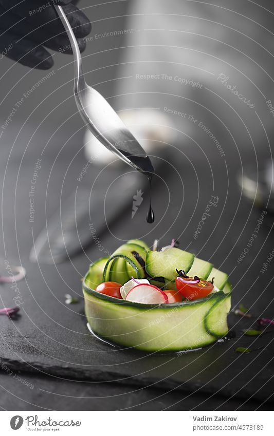 A vegetable salad made with fresh vegetables such as cucumber, tomato, feta cheese and microgreens. A gloved chef pours black sauce over a gourmet dish. Macro, selective food