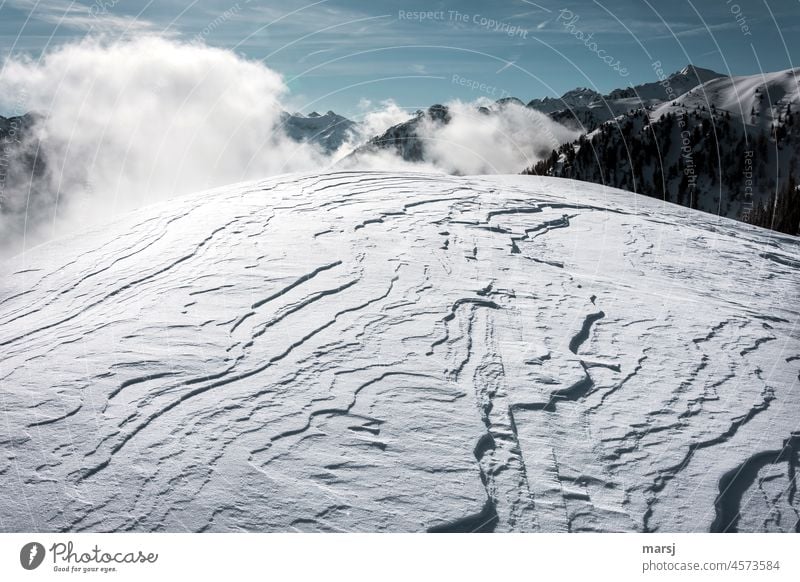 Snow cover formed by the wind. In the background snow-covered peaks and rising fog. Winter Uniqueness Alps Snowscape snowfield Nature Winter's day