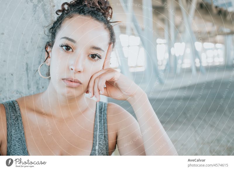 Portrait of tired looking serious young african woman taking a break after workout exercises. athlete female in sportswear relax hearing music on his phone. Urban sport .Leggings clothing and top.