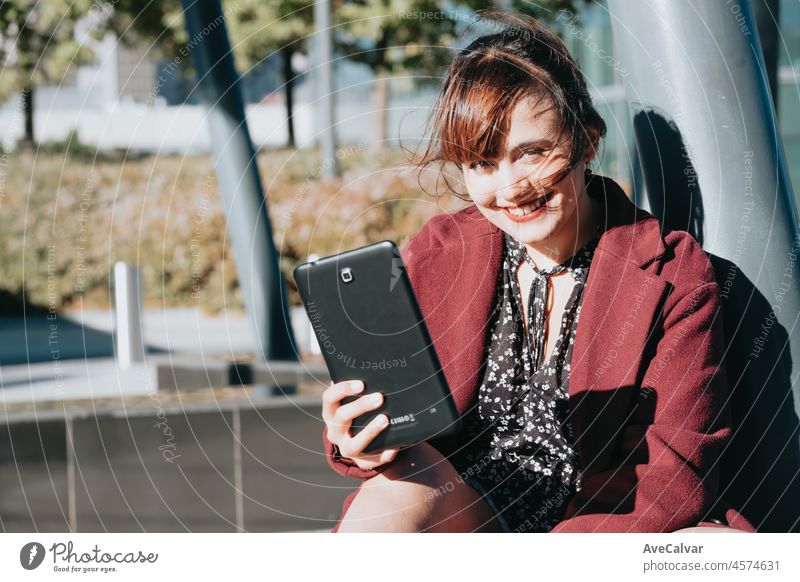 Elegant businesswoman standing outside office with digital tablet. Video call during free time at the work.Smiling pretty girl holding a digital tablet computer. Modern technologies, copy space.