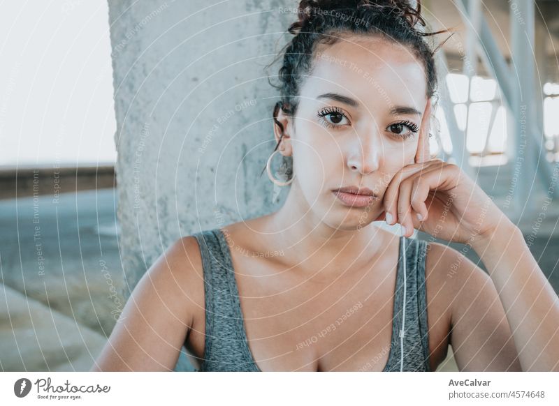 Close up Portrait looking serious young african woman taking a break after workout exercises. athlete female in sportswear relax hearing music on his phone. Urban sport .Leggings clothing and top.