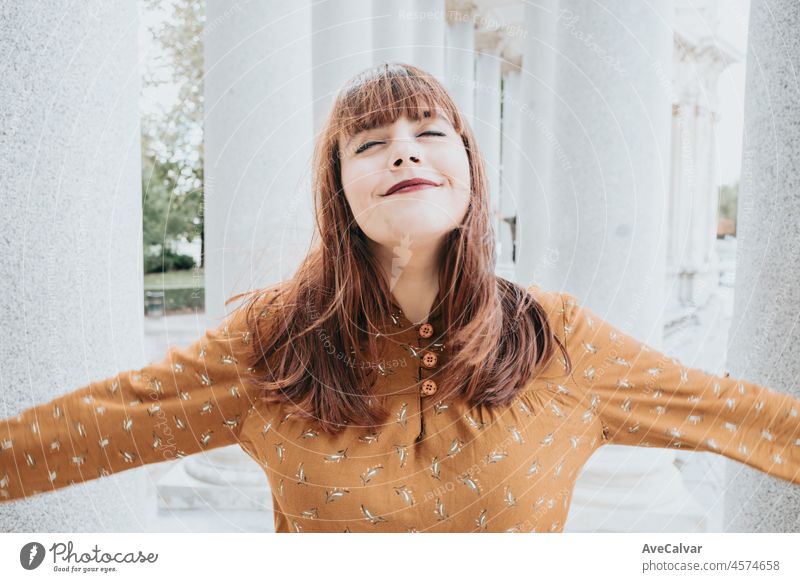 Portrait close up of a beautiful hipster caucasian woman closing eyes while smiling while hair is blowing moving wind outdoor. People and happiness concept. 80s vibes freedom and liberty.