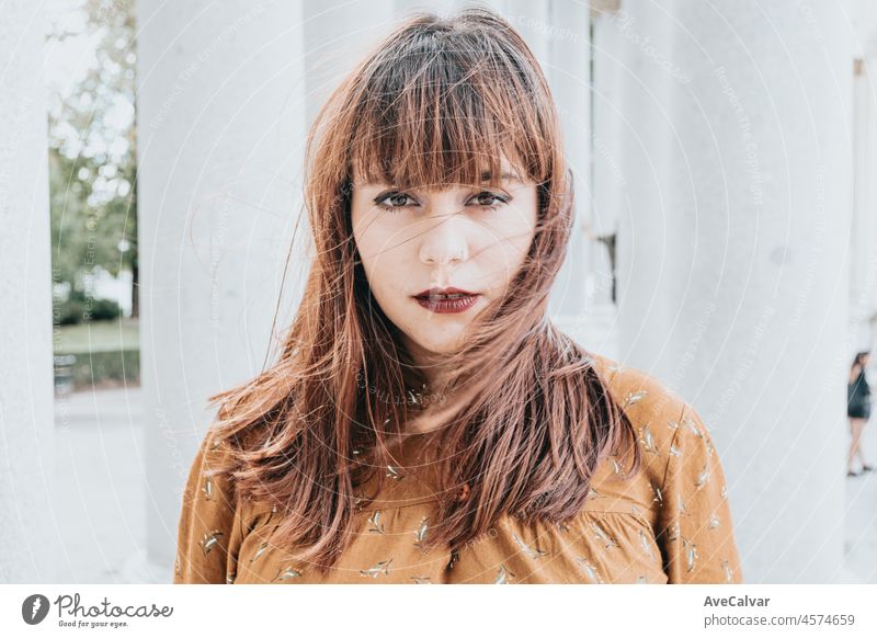 Portrait close up of a beautiful hipster caucasian woman looking serious to camera while the hair is blowing moving wind outdoor. People and happiness concept. 80s vibes