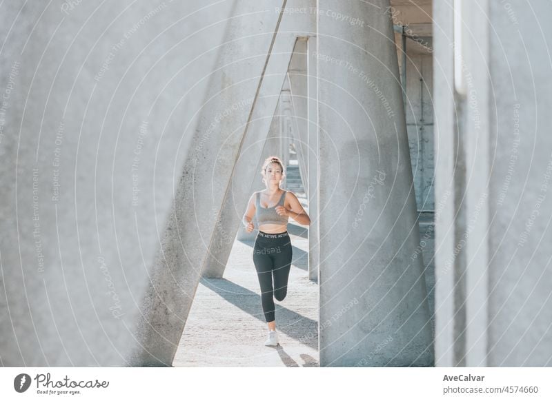 African american young athletic woman, curly hairstyle, running outdoors in the city, corridor Urban sports in the city. Sunset time with shadows. Serious woman concentrating in the competition train.