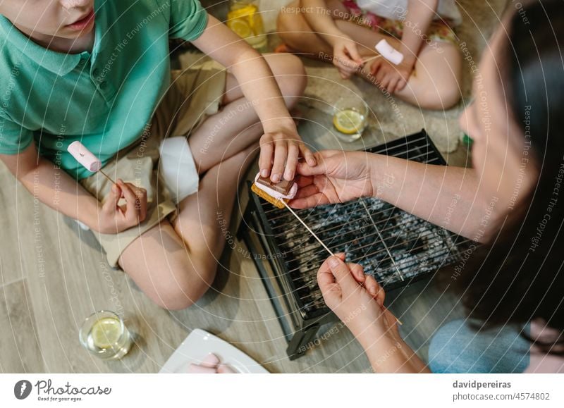 Top view of unrecognizable family making smores at home top view s'mores marshmallow chocolate cookie roasting small barbecue camping at home s mores boy girl