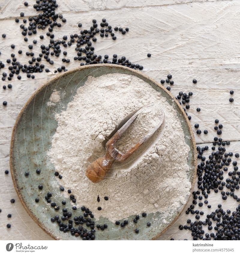 Plate with a scoop of black lentils flour and beans on white wooden table top view beluga alternative Legume raw dried plate spoon Black lentils uncooked