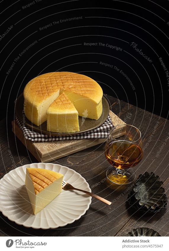 Japanese cheesecake with drink on table whole cake japanese cheese cake dessert food dim plate glass portion appetizing cotton dark obscure timber wooden lumber