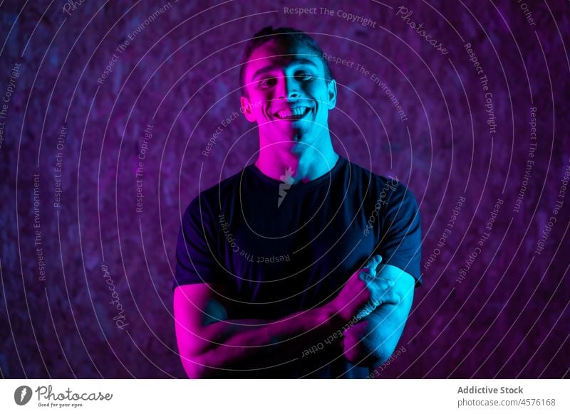 Cheerful male amputee under neon light man smile happy handicap illuminate purple bright portrait young friendly disable positive arms crossed cheerful