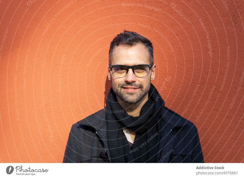 Delight male looking at camera against orange background in daytime man building street calm coat portrait city urban exterior pensive smile construction happy