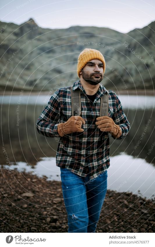 Man with cap and gloves in the mountains man hiker water shore tourist lake journey waterside nature ridge stone rough formation coast rocky waterfront festive