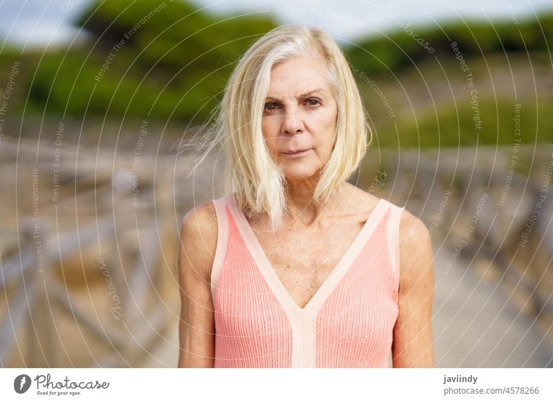 Eldery female walking along a wooden path near the beach., wearing a nice orange dress. mature woman senior old person lifestyle happy relaxing one tree pine