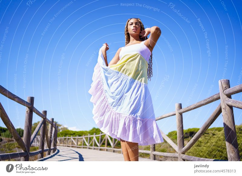 African female wearing a beautiful dress on a boardwalk on the beach. woman girl model zizi afrobraid braids fashion fashionable outdoors young person road