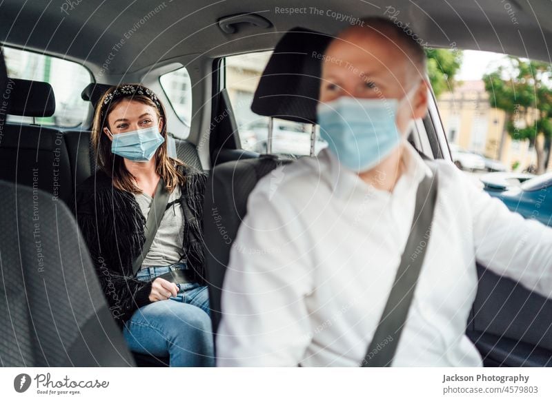 Taxi driver in a mask with a client on the back seat wearing mask uber taxi car passenger caucasian travel woman distance ride protect surgical mask viral adult