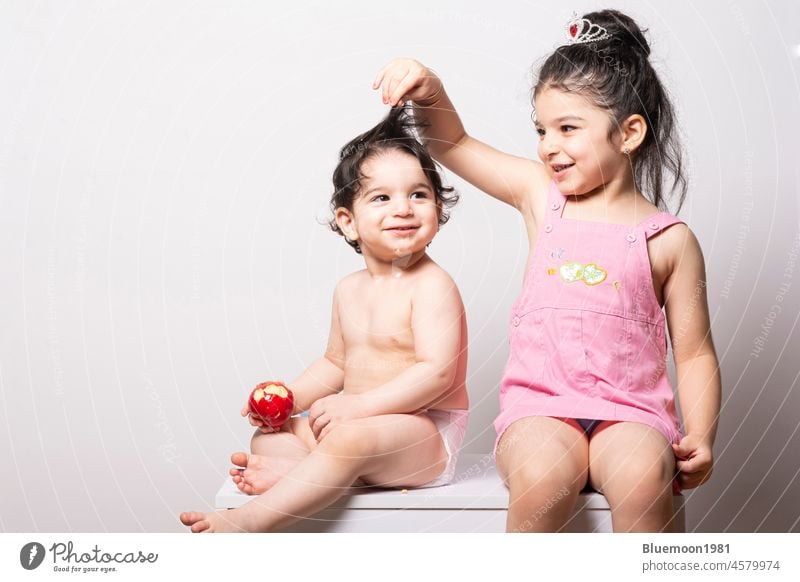 One year old baby with diaper beside her sister-joy and cheerful moments family fun girl Caucasian eating apple nutrition red food seat one face adorable alone