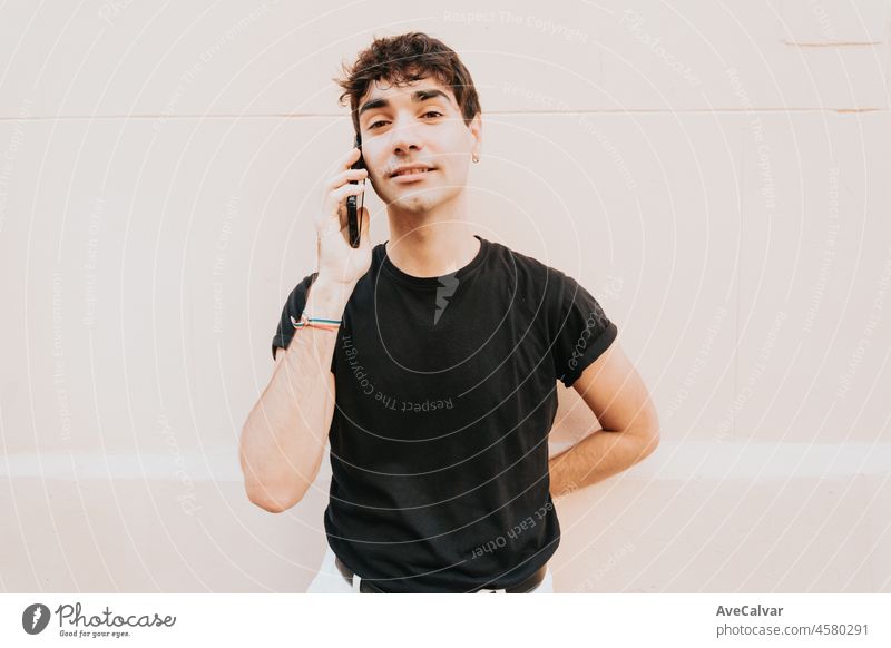 Handsome male with short hair in a black shirt making a call on his mobile smart phone in the city street. Copy space. Wall background. Looking serious to camera thinking about something