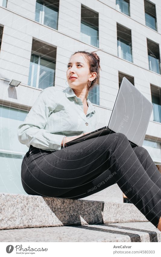 Young african american Businesswoman sitting on steps outdoors working on laptop during a bright day. Successful freelancer typing on keyboard using laptop computer. Portrait of woman copywriter