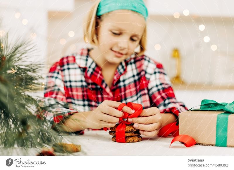 A pretty girl decorates cookies with a bright red ribbon, prepares a sweet treat for guests on Christmas or New Year's Eve christmas gift new year surprise