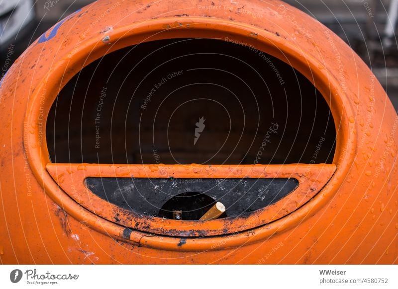 A cigarette butt is stuck in an orange public trash can in Berlin streetscape waste Smoking Cigarette tilt Cigarette Butt Dirty filth Trash rubbish bin Street