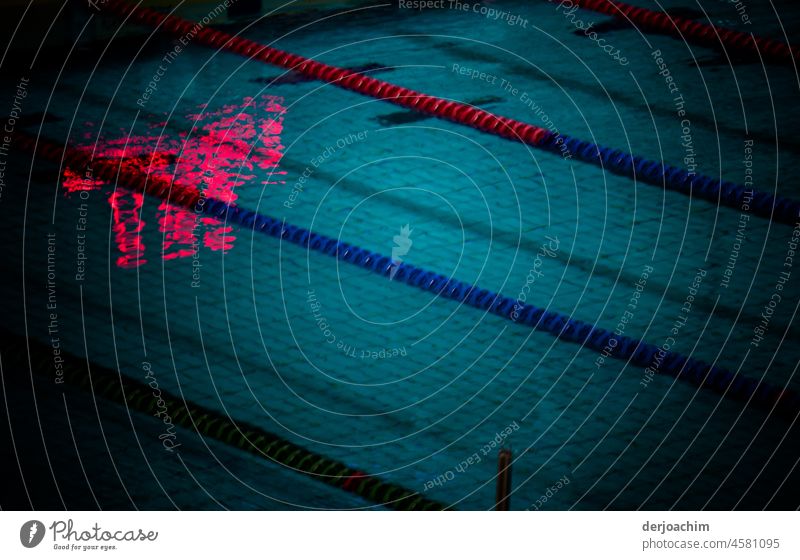 Reflection & reflection in the pool. Blue water. Marked swimming lanes and from the ceiling a red eerie structure that is reflected in the water. Swimming pool