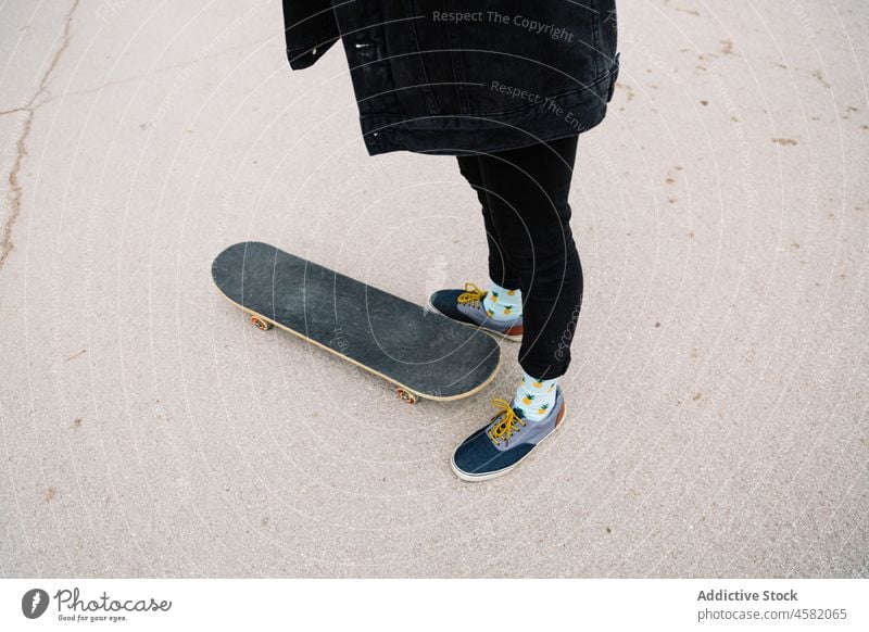 Crop person in sneakers standing near skateboard on asphalt road skater city street urban pavement casual jeans active activity leg free time subculture rest