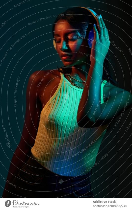 Brazilian woman in headphones in studio with shadows style trendy dance fluorescent music ultraviolet disco ball portrait song meloman eyes closed modern light