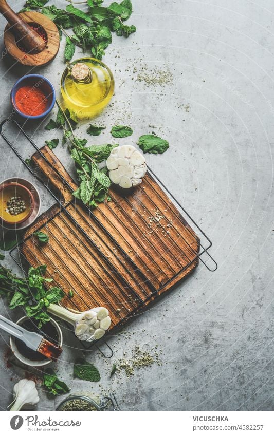 Food background with cutting board and various healthy flavor seasoning ingredients: herbs, garlic, olive oil, chili powder and pepper. Cooking at home with flavorful spice. Top view. Border