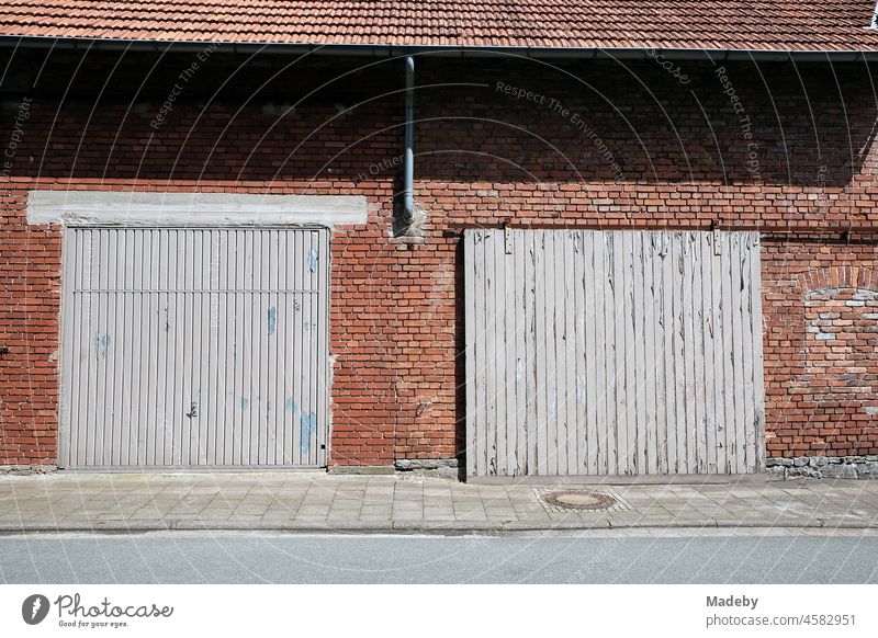 Old grey wooden gates in front of a stable and barn made of red brick in summer sunshine on a farm in Alverdissen near Barntrup in East Westphalia-Lippe Farm