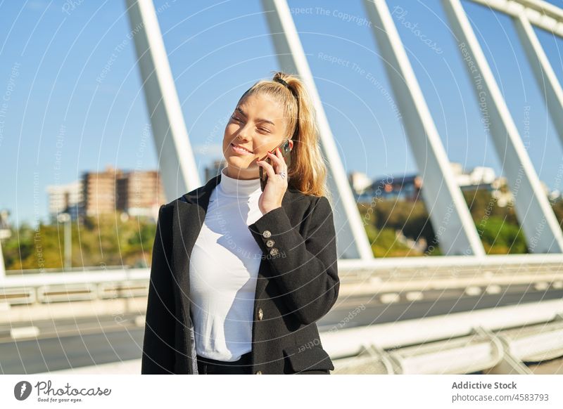 Young woman talking on mobile phone on bridge in sunlight smartphone city gadget using cellphone device road speak street conversation urban asphalt backpack