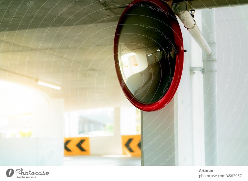 Convex safety mirror at curve of indoor car parking lot to reduce risk of accidents from blind corner or blind spots. Convex circular safety mirror in multi-level parking garage. Indoor traffic convex