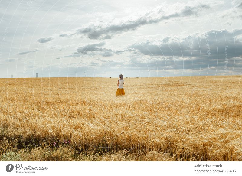 Anonymous woman standing in wheat field nature countryside summer rural skirt natural plantation female brunette calm sky cloudy peaceful meadow lady short hair