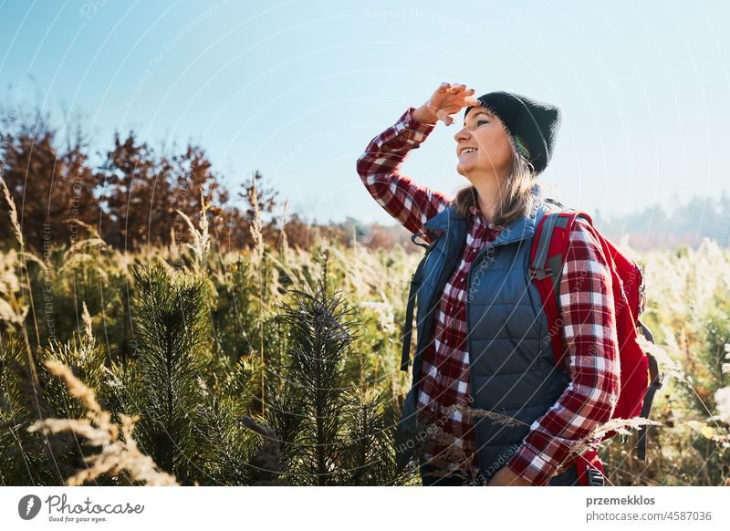 Young woman enjoying the view of mountains. Woman standing on trail and looking at view. Woman with backpack hiking through tall grass along path in mountains