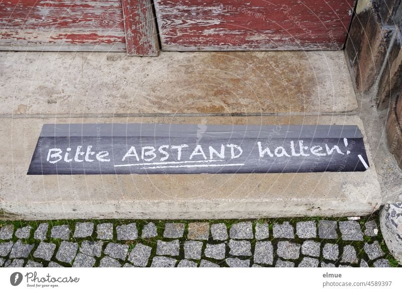 Please keep your distance - standing on the ground in front of an old wooden door of an old building / Corona containment ordinance. please keep your distance