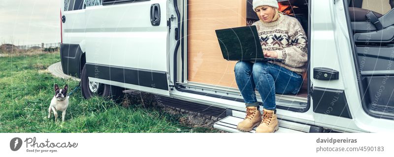 Woman teleworking sitting in the door of a camper van woman telecommuting laptop banner web panorama panoramic header copy space trip tablet remote work people